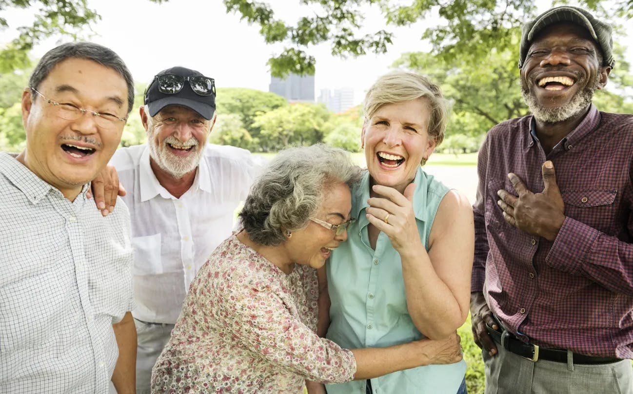 Five older people laughing together in a park