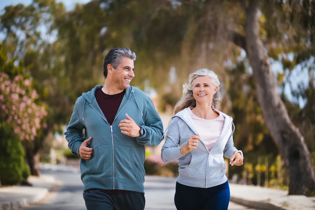 Man and woman jogging and smiling down treelined street