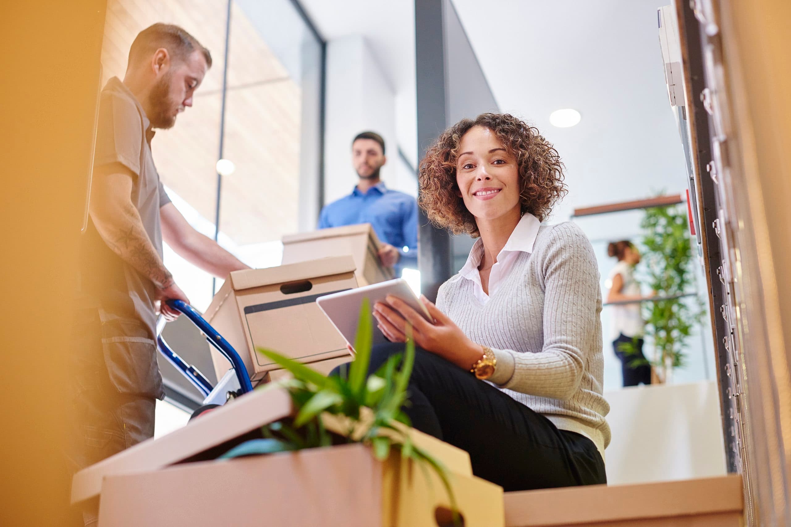 Woman smiles at camera while packing up her office for a job change