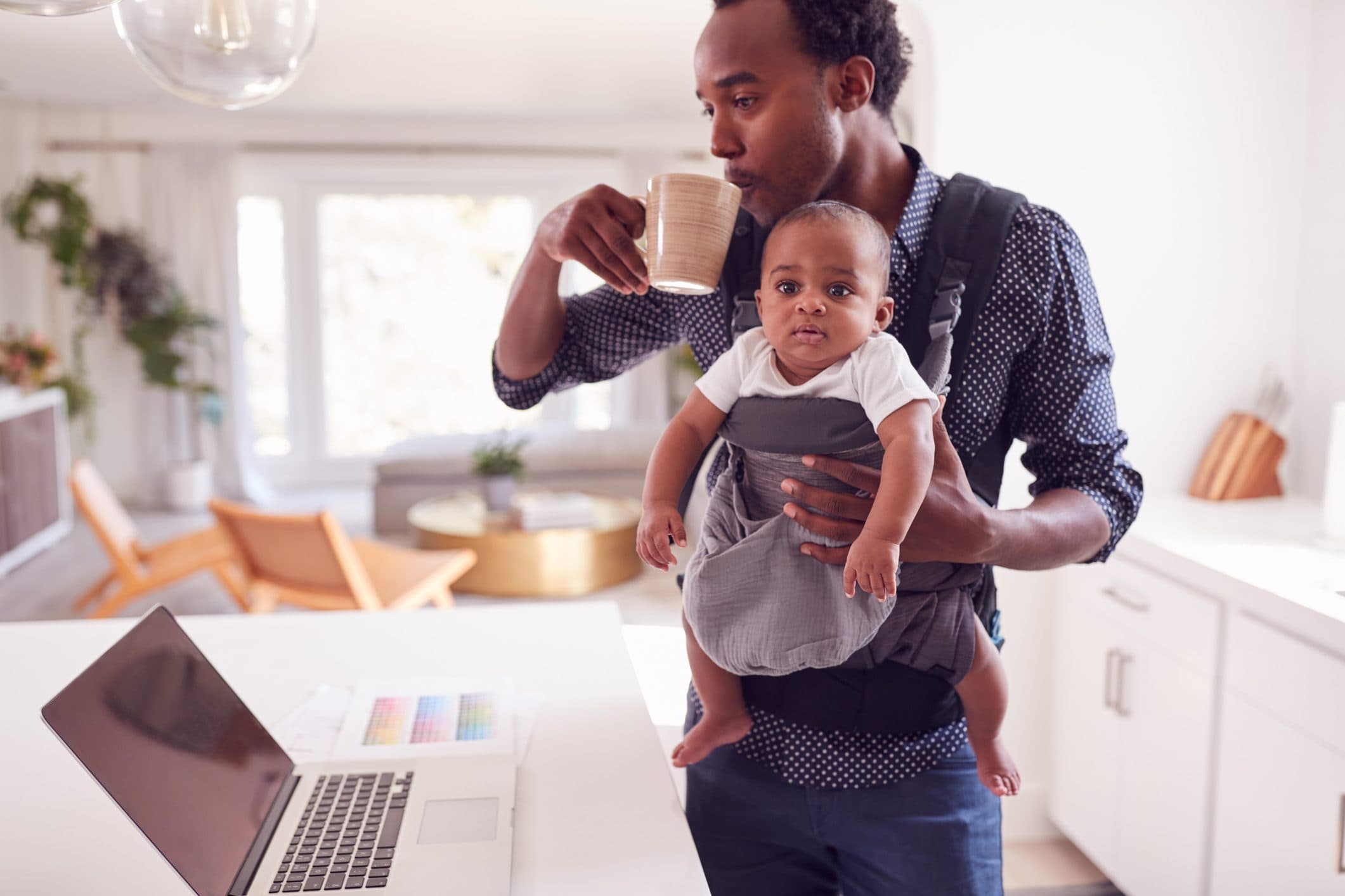 Father carrying his baby while drinking coffee at home