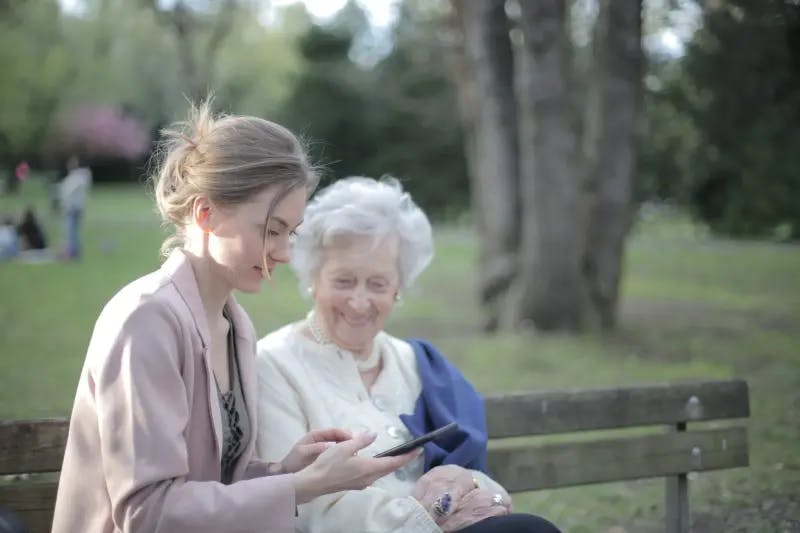 Older woman and younger woman sitting on a park bench looking at a phone