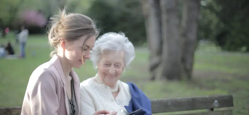 Older woman and younger woman sitting on a park bench looking at a phone