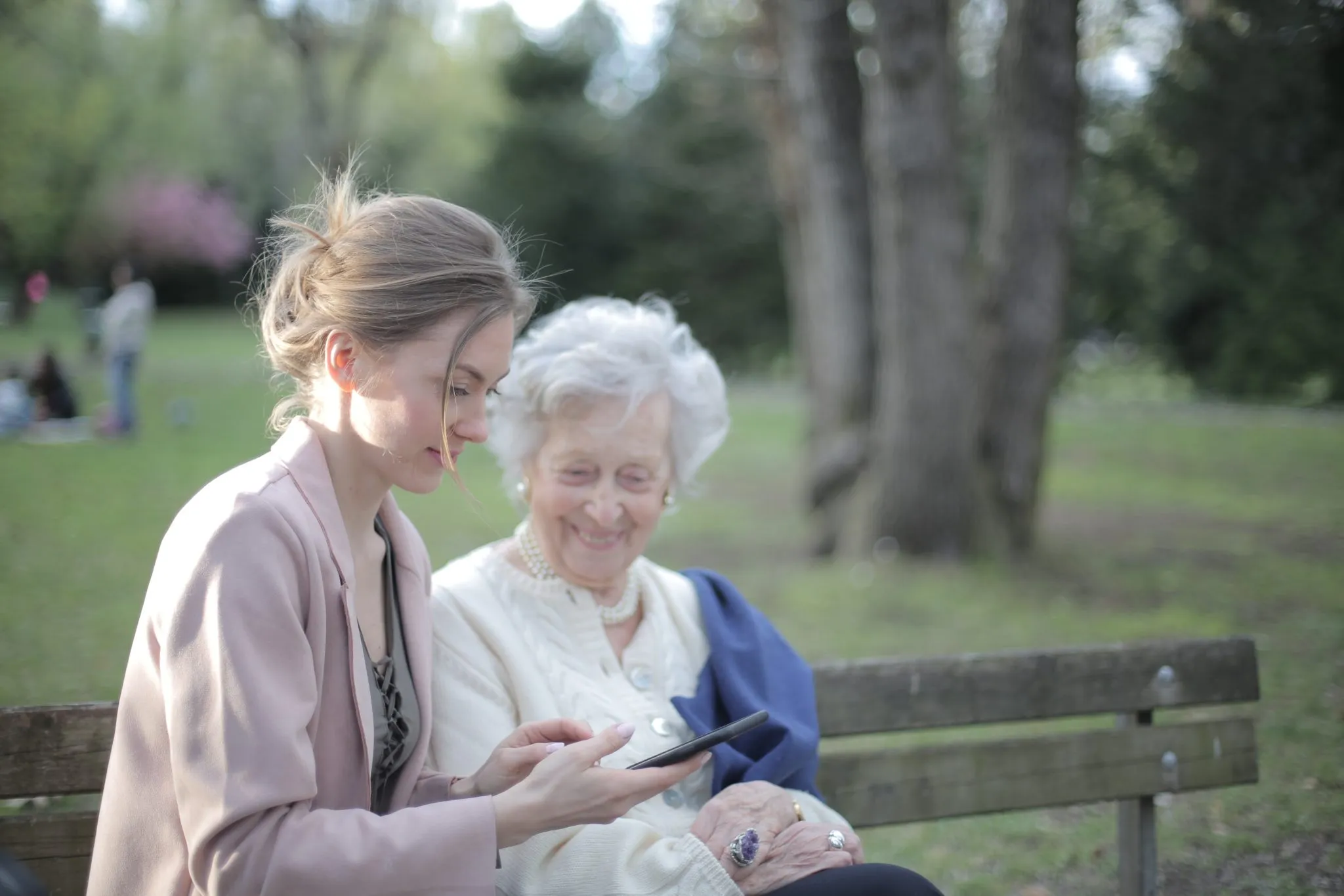Older woman and younger woman sitting on a park bench looking at a phone