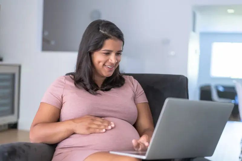 Pregnant woman sitting in a chair and using a laptop