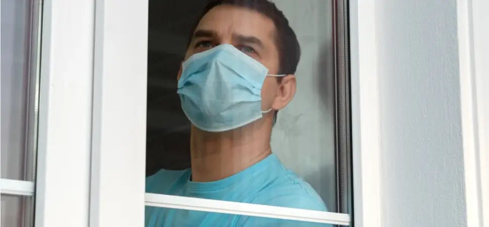 Person wearing a mask looking out a window