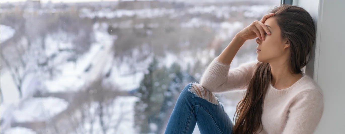 Woman covering her eyes beside a window in winter