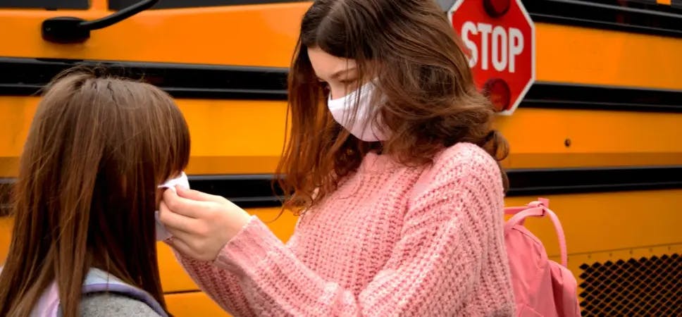 People wearing masks in front of a school bus