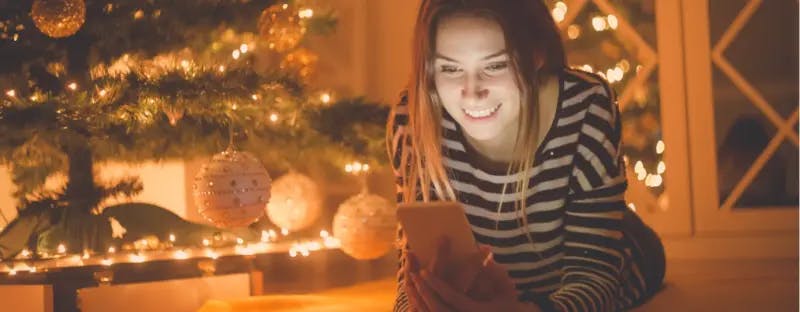 Person looking at a smartphone beside a Christmas tree