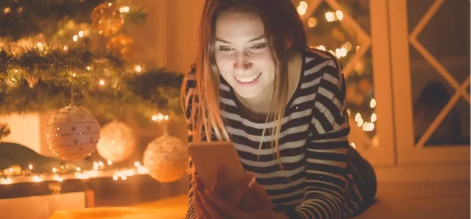 Person looking at a smartphone beside a Christmas tree