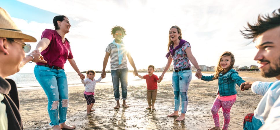 View point of young families dancing at beach on ring around the rosy style - Lifestyle joy concept with mixed race people having fun moment holding hands