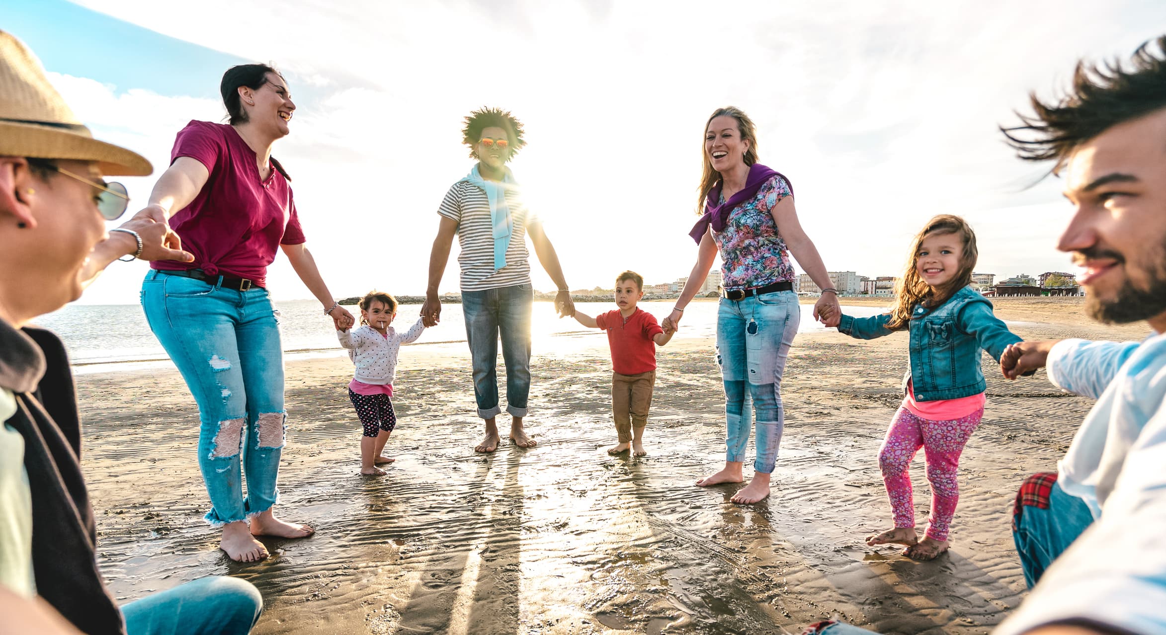 View point of young families dancing at beach on ring around the rosy style - Lifestyle joy concept with mixed race people having fun moment holding hands - Vivid backlight filter with sunshine halo stock photo