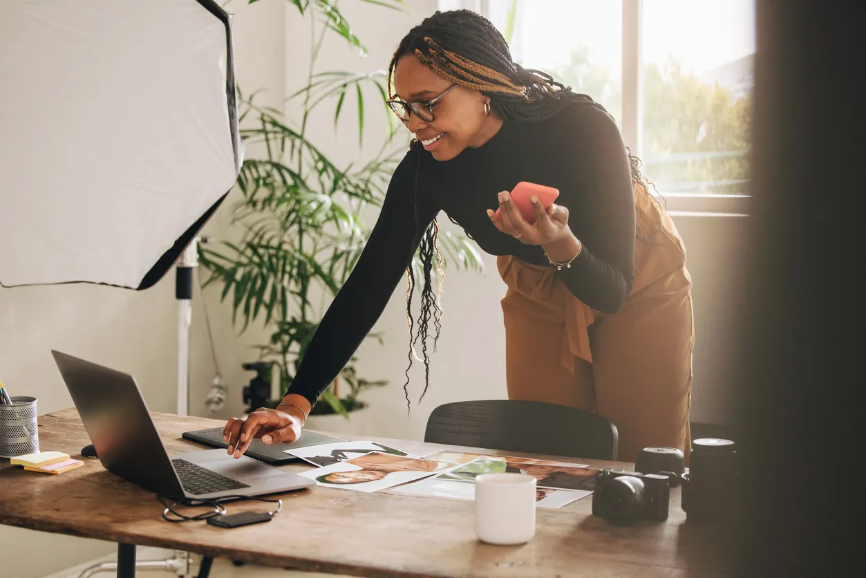 Woman standing over an office desk using a laptop and holding a phone