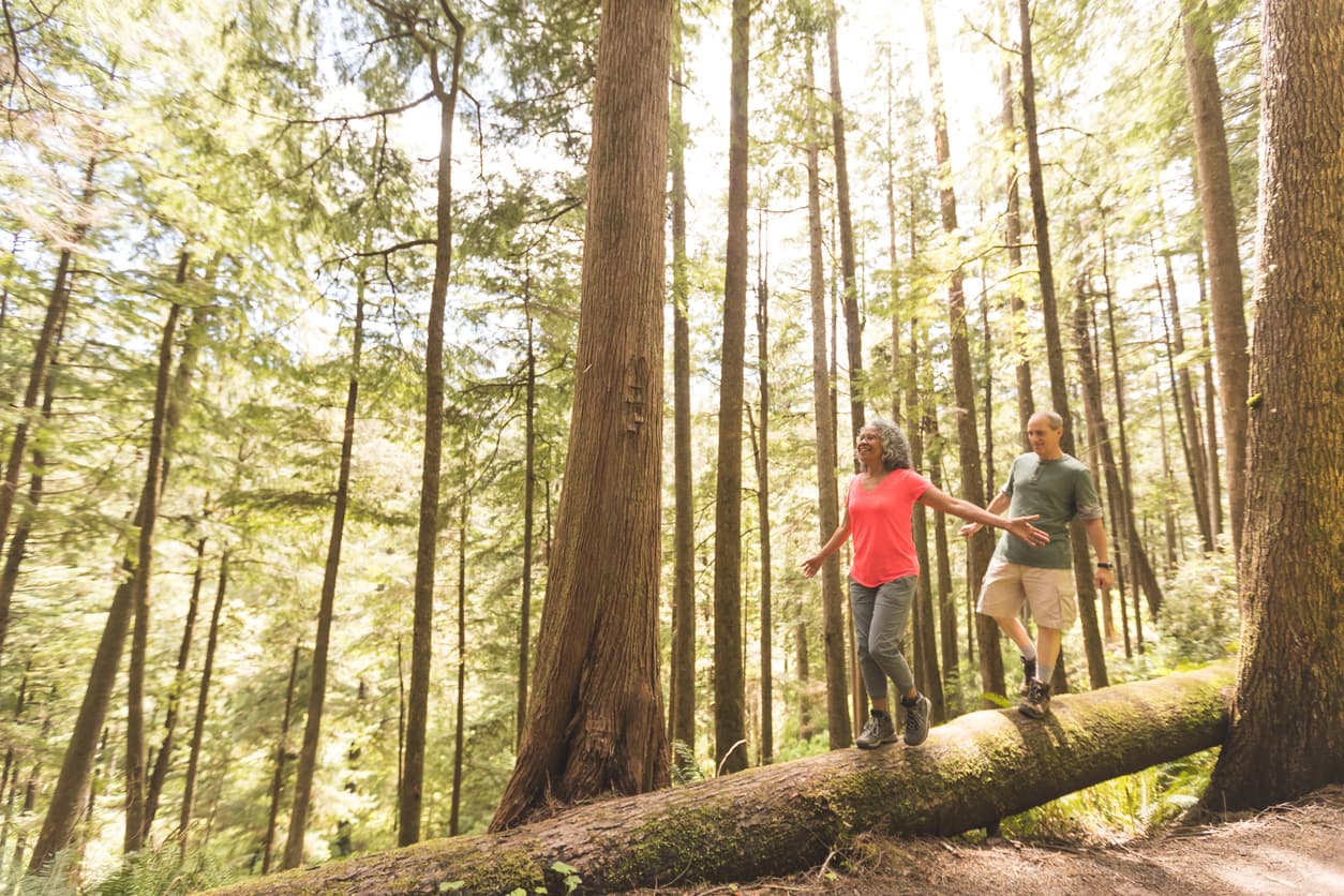 A couple walks on a log in the woods while hiking