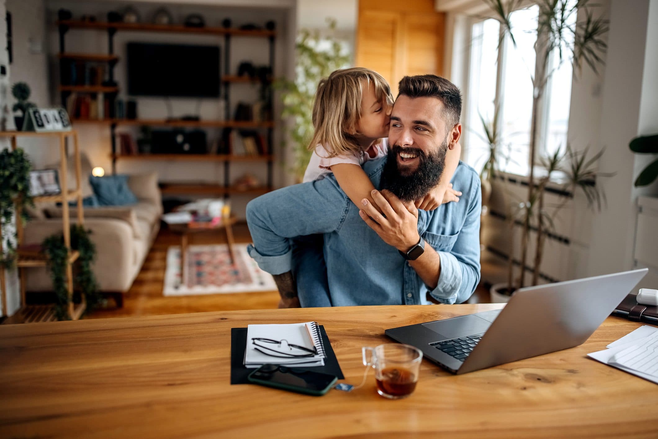 Father working at a laptop while his daughter hugs him