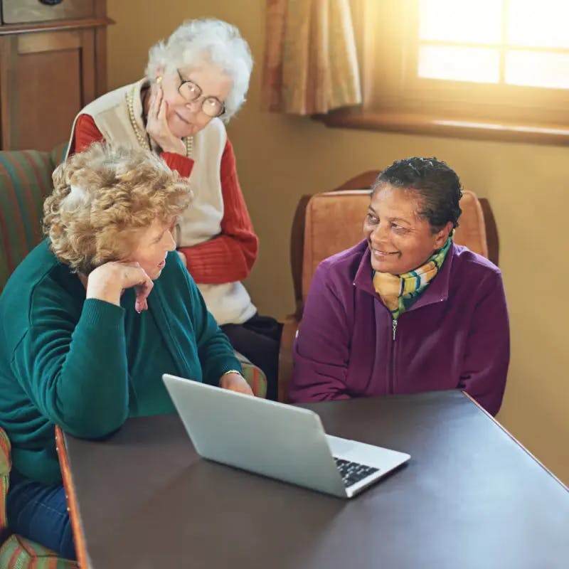Three older women at a desk with a laptop