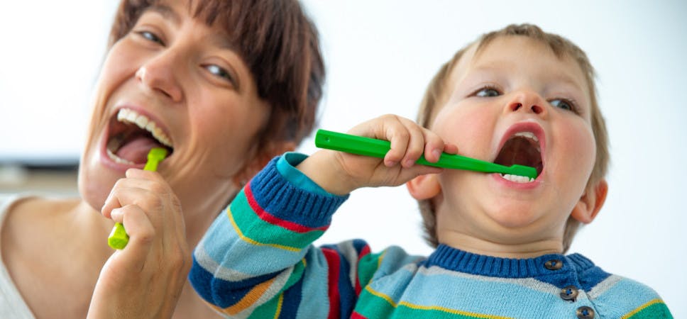Happy Mother and Son Enjoying Brushing Teeth Together Against White Background