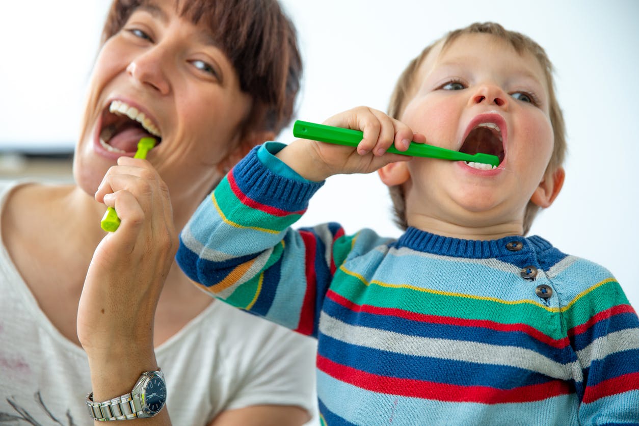 Happy Mother and Son Enjoying Brushing Teeth Together Against White Background