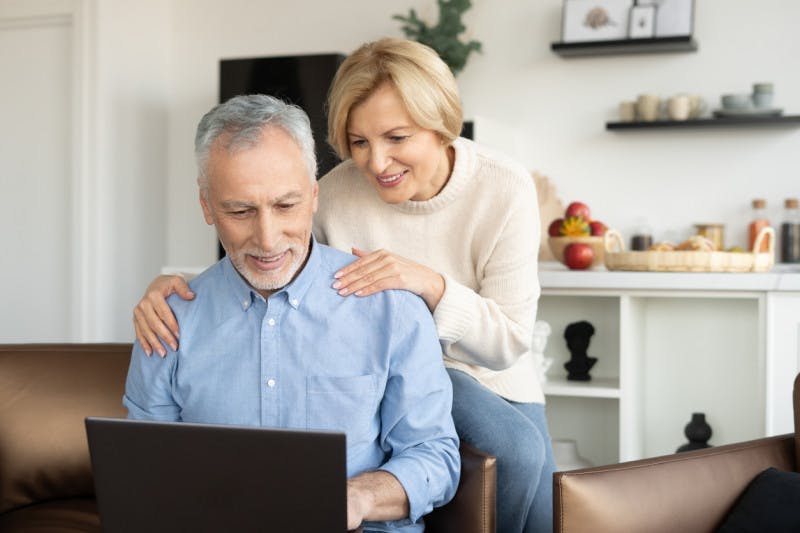 A male and female middle aged smiling couple looking at the computer 