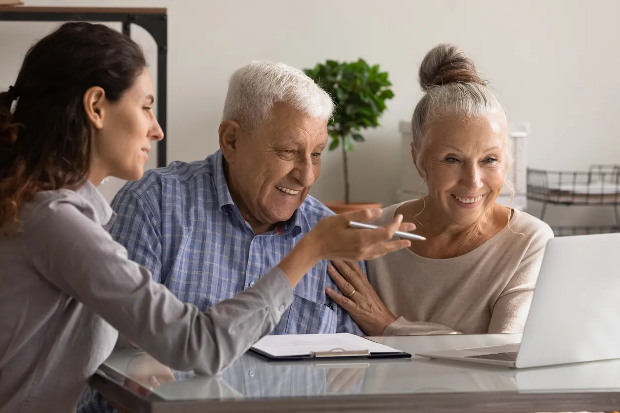 Older couple with a younger woman at a desk with clipboard and laptop