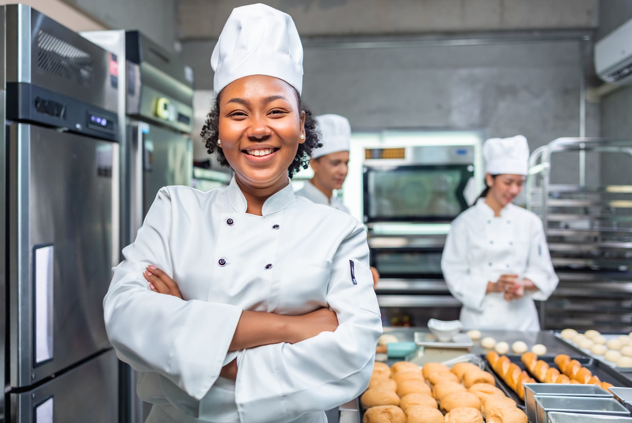 African American woman bakers looking at camera..A chef baker in a chef's dress and hat, cooking together in the kitchen. She takes fresh-baked cookies out of the modern electric oven in the kitchen.